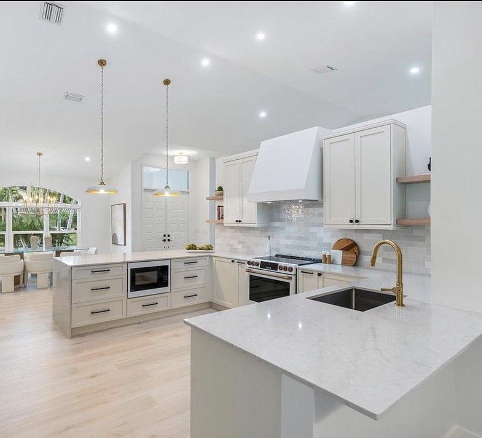 The client's open-plan white kitchen with island, gold fixtures and pendant lighting, the bright dining/sunroom visible